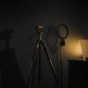 HeyGen AI video concept - an empty camera tripod and ring light in a dark studio lit only by a laptop glow